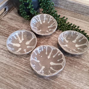 May include: Four small, gray ceramic bowls with white glaze. The bowls have a unique, textured design and are arranged on a wooden surface.