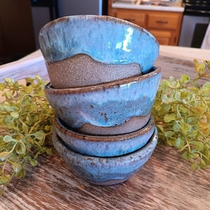 May include: A stack of four handmade ceramic bowls with a blue and brown glaze. The bowls are stacked on a wooden surface.