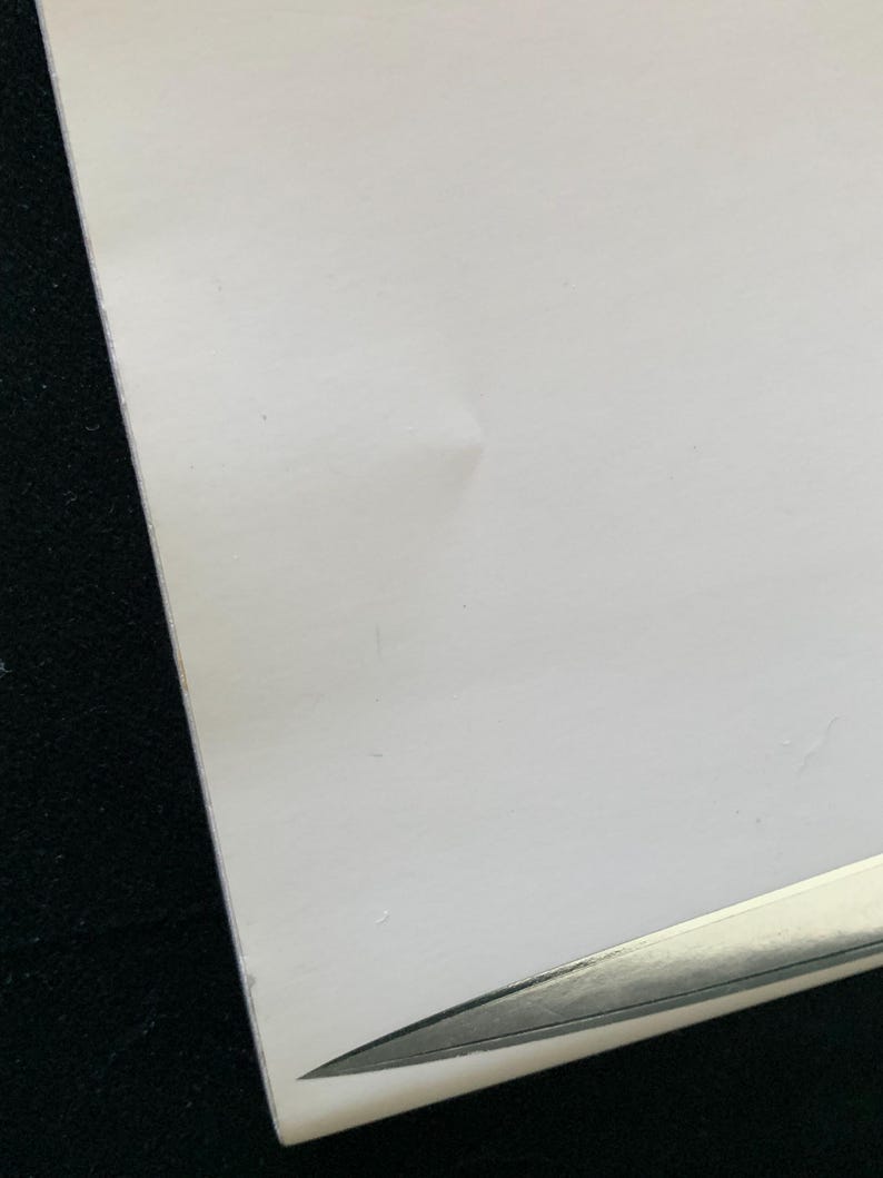Puede incluir: Primer plano de un papel blanco con una ligera arruga y un objeto plateado en la esquina. El papel tiene una textura suave y est&aacute; sobre un fondo oscuro.