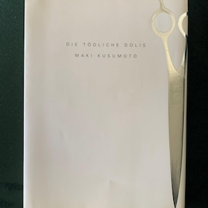 Puede incluir: Portada de libro con el t&iacute;tulo "DIE T&Ouml;DLICHE DOLIS" y el autor "MAKI KUSUMOTO" en texto negro. Un gr&aacute;fico de tijeras de peluquer&iacute;a plateadas est&aacute; en el lado derecho de la portada. El fondo es blanco.