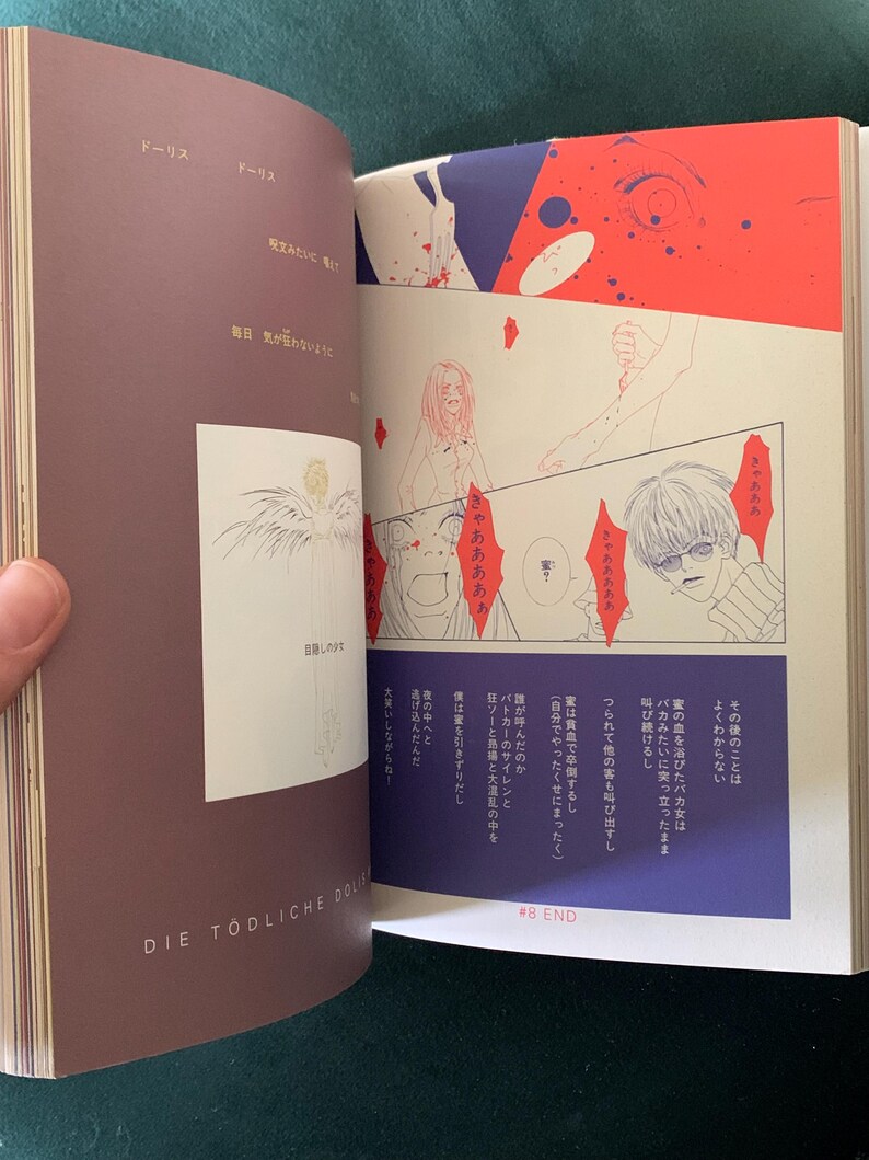 Puede incluir: Libro abierto con ilustraciones de manga japon&eacute;s. Las p&aacute;ginas presentan paneles con bocadillos, dibujos de personajes y texto japon&eacute;s. La portada es de color marr&oacute;n oscuro con el t&iacute;tulo "DIE T&Ouml;DLICHE DOLL" impreso.
