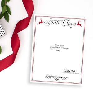 May include: A white card with a red border and black text that reads "From the Desk of Santa Claus". There are two red reindeer illustrations on the card. The text "Type your Christmas message here" is written in black. The card is on a white surface with a red ribbon, a black and white polka dot gift box, and green leaves.