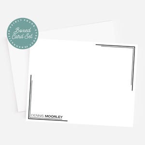 May include: A white card set with black border accents and the name "DENNIS MOORLEY" printed at the bottom. A teal circular sticker with the words "Boxed Card Set" is in the upper left corner. The set includes a white envelope.