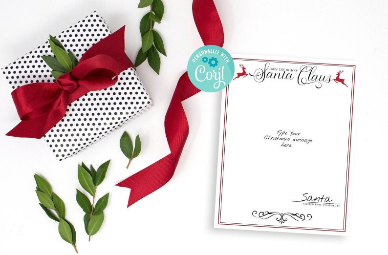 May include: A white card with a red border and the text "From the desk of Santa Claus" in black cursive. There are two red reindeer illustrations on the card. The card is on a white surface with a red ribbon, a gift wrapped in black and white polka dot paper, and green leaves.