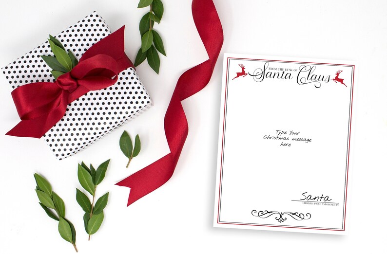 May include: A white card with a red border and black text that reads "From the Desk of Santa Claus". There are two red reindeer illustrations on the card. The text "Type your Christmas message here" is written in black. The card is on a white surface with a red ribbon, a black and white polka dot gift box, and green leaves.