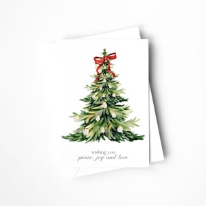May include: A white greeting card featuring a watercolor illustration of a green Christmas tree decorated with small white ornaments and a red bow at the top. The text below the tree reads, wishing you peace, joy and love.