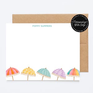 Op de afbeelding: Wit briefpapier met de naam "Poppy Summers" in turquoise. De onderkant van het briefpapier toont aquarel illustraties van kleurrijke strandparasols. Het briefpapier wordt gecombineerd met een bruine envelop.