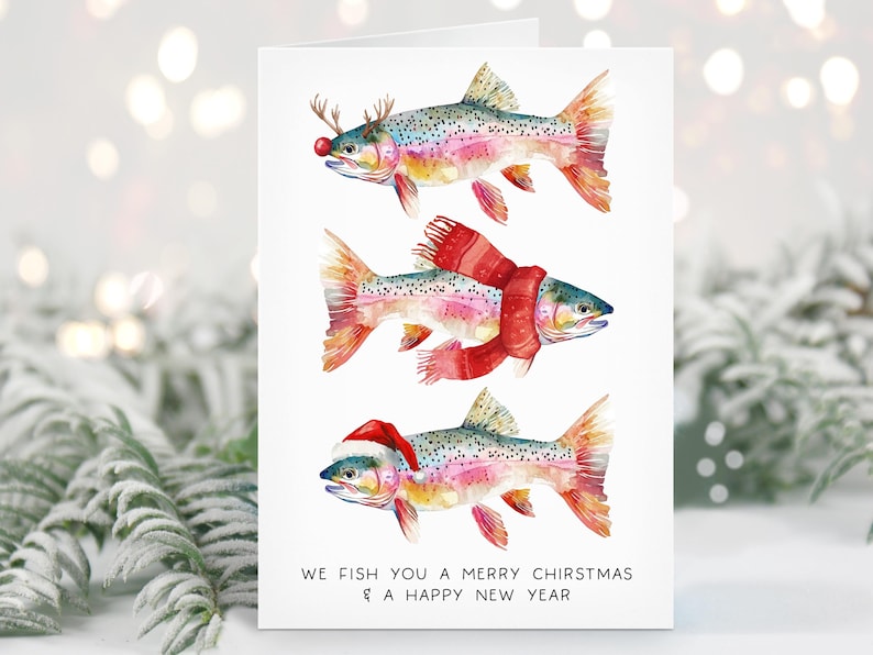 May include: A Christmas card featuring watercolor illustrations of rainbow trout decorated with festive accessories. One fish wears reindeer antlers and a red nose, another a scarf, and the last a Santa hat. The text reads "We fish you a Merry Chiristmas & a Happy New Year."