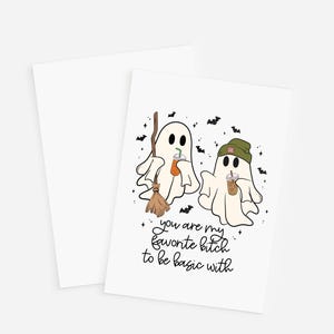 May include: A white greeting card featuring a cartoon illustration of two ghosts. One ghost holds a broom and an orange drink, while the other wears a green beanie and holds a brown drink. Black bats and stars surround them with the text: you are my favorite bitch to be basic with.
