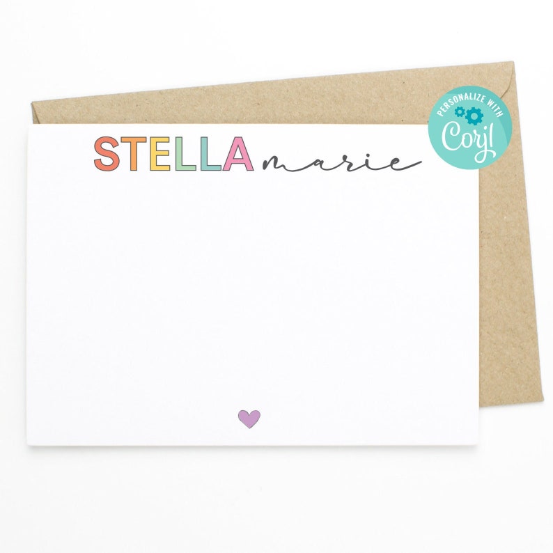 May include: A white card with a rainbow colored name "STELLA marie" written on it. The card has a small purple heart in the bottom center. The card is on top of a brown envelope with a blue circle sticker that says "Personalize with Cory!" with a gear icon.