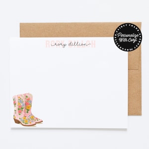 May include: A white stationery set with a floral cowboy boot design. The set includes a blank card with the name "Rory Dillion" and a brown envelope. A black circular sticker reads "Personalize With Corjl".