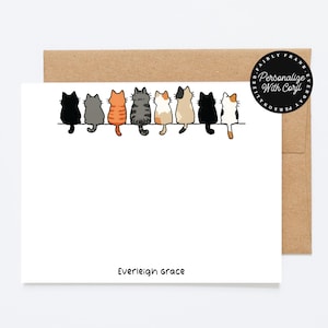 Può includere: Una carta bianca con una busta marrone presenta una fila di gatti dei cartoni animati in vari colori. Il testo "Everleigh Grace" è stampato in basso. Un adesivo circolare sulla busta recita "Personalize With Corjl".
