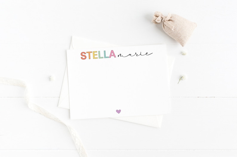 May include: A white card with the name "STELLA marie" written in rainbow letters. A small purple heart is at the bottom of the card.