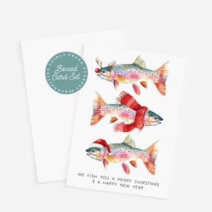 May include: A boxed card set featuring watercolor illustrations of fish decorated for Christmas. One fish wears reindeer antlers, another a scarf, and the third a Santa hat. The text reads "We fish you a merry Christmas & a happy new year."