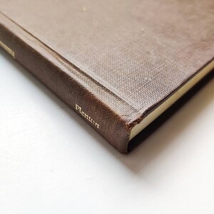 Puede incluir: Primer plano de un libro marr&oacute;n con letras doradas en el lomo y la portada. El libro tiene una cubierta texturizada y la palabra "Plenum" es visible en dorado. Las p&aacute;ginas tienen un tono amarillo claro.