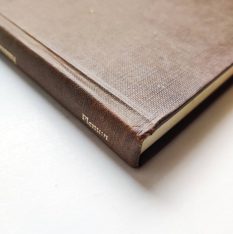 Puede incluir: Primer plano de un libro marr&oacute;n con letras doradas en el lomo y la portada. El libro tiene una cubierta texturizada y la palabra "Plenum" es visible en dorado. Las p&aacute;ginas tienen un tono amarillo claro.