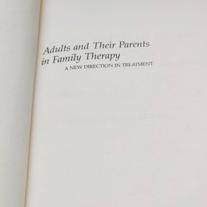 Puede incluir: P&aacute;gina de libro abierta con el t&iacute;tulo "Adults and Their Parents in Family Therapy" en negro. El subt&iacute;tulo dice "A New Direction in Treatment". La p&aacute;gina es blanca.