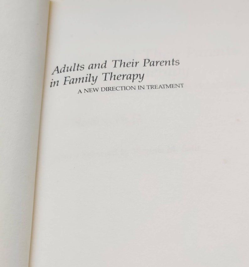 Puede incluir: P&aacute;gina de libro abierta con el t&iacute;tulo "Adults and Their Parents in Family Therapy" en negro. El subt&iacute;tulo dice "A New Direction in Treatment". La p&aacute;gina es blanca.