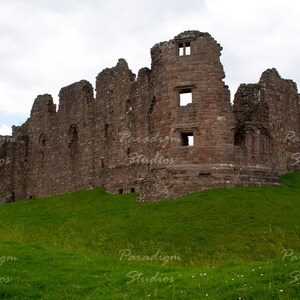 May include: Ruins of a stone castle on a grassy hill. The castle is made of brown stone and has several towers. The sky is cloudy.