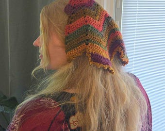 May include: A triangular crochet headscarf featuring a chevron pattern in earthy tones of mustard yellow, forest green, deep purple, and burnt orange. The accessory is crafted with a textured yarn stitch and has a scalloped edge along the bottom border.