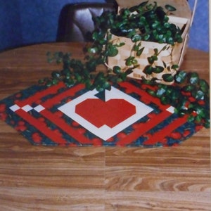 May include: A red, white, and green table runner with a heart design. The table runner is called "Apple Array Table Runner #935" and is part of the "Stitch'n Friends" collection.