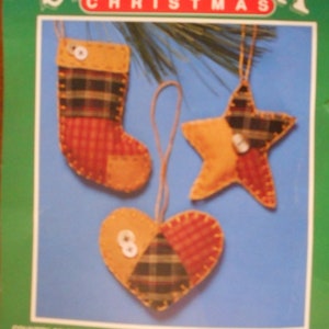 May include: A craft kit for making three Christmas ornaments: a stocking, a star, and a heart. The ornaments are made of patchwork fabric in red, green, and brown with a plaid pattern. The kit is by Bernat.