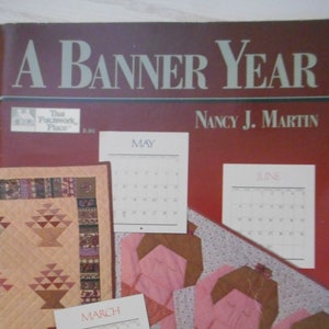 以下が含まれることがあります： ナンシー・J・マーティン著「A Banner Year」というタイトルの本。パッチワークキルトのデザインと、1年間の各月のカレンダーが掲載されています。