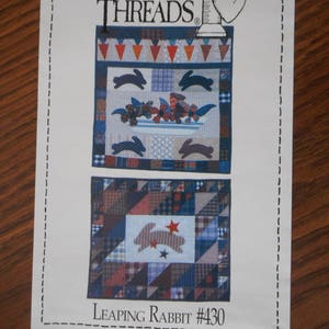 May include: A quilting pattern from Country Threads titled "Leaping Rabbit #430". The pattern features two quilt designs with a patchwork style and a bunny motif. The designs are in shades of blue, red, brown, and white.