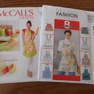 Può includere: Due buste di modelli di cucito McCall's. Uno presenta accessori da cucina con una donna che indossa un grembiule con disegni di frutta. L'altro mostra disegni di grembiuli. Il testo "McCall's Crafts" e "McCall's Fashion Accessories" è visibile.