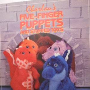 May include: A book titled "Charlou's Five-Finger Puppets and Stuffed Toys" by Charlou Baker Dolan. The cover features a colorful illustration of four puppets: a red dragon, a brown bear, a purple monster, and a blue dragon.