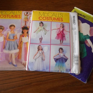 Puede incluir: Tres patrones de costura para disfraces de hada. Los patrones son de McCall's y Simplicity. Los patrones de McCall's muestran a niñas usando diferentes disfraces de hada con alas. El patrón de Simplicity muestra a una niña usando un disfraz de hada verde con alas rosadas.