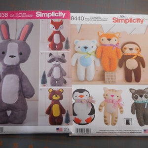 May include: Two Simplicity sewing patterns for making stuffed animals. The pattern on the left is S8938 and features a gray bunny with white accents. The pattern on the right is 8440 and features a variety of animals including a penguin, a raccoon, a fox, a bear, a cat, and a sloth.
