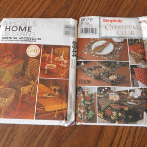 Op de afbeelding: Twee naaipatronen voor thuisdecoratie. Het patroon aan de linkerkant is McCall's Home Decorating, patroonnummer 8944, en heeft een geruite stoel en een tafelkleed. Het patroon aan de rechterkant is Simplicity Christmas Club, patroonnummer 9979, en heeft een verscheidenheid aan kerstthema tafelkleden, placemats en een mand.