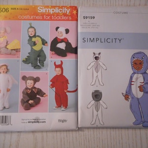 May include: Two sewing patterns for toddler costumes. The pattern on the left is Simplicity 2506 and includes costumes for a dragon, angel, devil, monkey, and elephant. The pattern on the right is Simplicity S9159 and includes costumes for a shark and a dog.