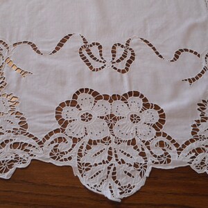 May include: White cotton table runner with intricate cut-out floral design. The design features delicate flowers and leaves, creating a lacy effect.