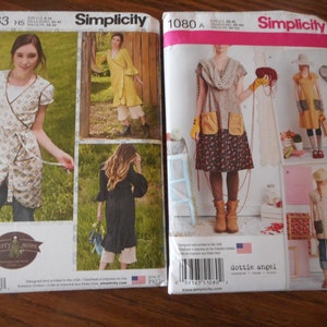 May include: Two Simplicity sewing pattern envelopes. The envelope on the left is for pattern number 8763 and features a woman wearing a floral wrap dress. The envelope on the right is for pattern number 1080 and features a woman wearing a floral dress with pockets and a crocheted scarf.