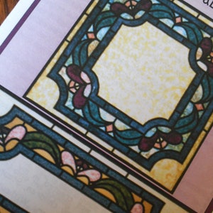 May include: Two stained glass window designs with a floral motif. The designs are in shades of blue, green, yellow, pink, and purple. The designs are framed in black.