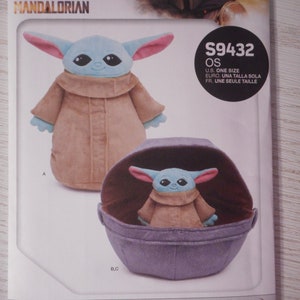 May include: A Simplicity sewing pattern for a plush Grogu toy and a soft space pram. The pattern is for one size and includes instructions for making both the toy and the pram. The pattern is from Star Wars: The Mandalorian.