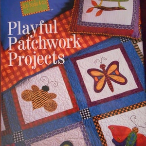 May include: A book titled "Playful Patchwork Projects" by Kari Pearson & Friends. The cover features a patchwork quilt with squares showcasing insect and butterfly designs. The quilt has a blue, red, and orange color scheme.