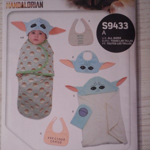 May include: A sewing pattern for a baby costume inspired by the Star Wars character, The Child, also known as Baby Yoda. The pattern includes instructions for making a hooded towel, a bib, and a hat with ears. The pattern is for all sizes and is available in English, French, and Spanish. The pattern is from Simplicity.