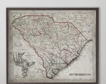 May include: Framed vintage map of South Carolina, featuring detailed cartography with red and green accents. The map includes the text "South Carolina" and a smaller inset map of Charleston. The frame is a dark, neutral color.