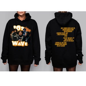 May include: Black hoodie with a yellow graphic print of the words "Rod Wave" and a group of people. The back of the hoodie has yellow text that reads "See I done been lied to, backstabbed and heartbroken. I wanted to cry, but I was to afraid to open. Prayin' one day, I'd find a peace of mind by the ocean. I spent all my time committing crimes to get closer."
