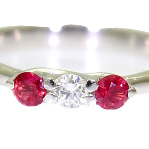 May include: A silver band ring set with three stones. The centre stone is a clear diamond, and the two stones on either side are red rubies.