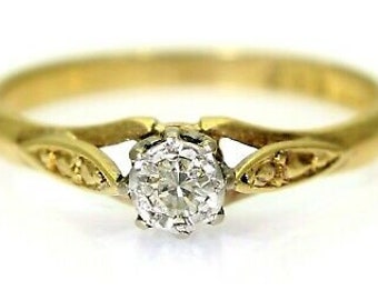 May include: A gold band ring with a single round diamond set in a prong setting. The band has a delicate, ornate design.