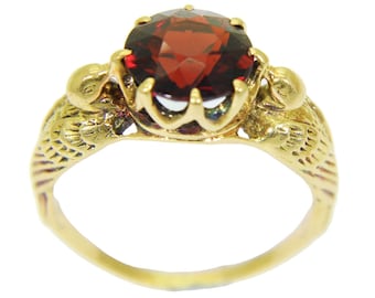 May include: A gold ring with a large, round, red gemstone set in a decorative, ornate setting. The ring features a design of two birds on either side of the stone.