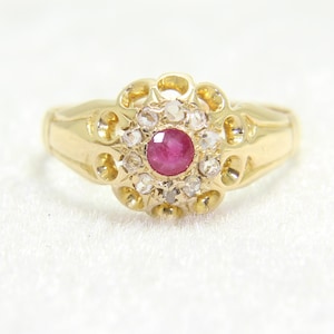 Può includere: Un anello d'oro con un rubino centrale e un alone di pietre preziose chiare. L'anello presenta un motivo floreale con una fascia lucida. Le pietre preziose sono incastonate in un'incastonatura ornata. Il design dell'anello ricorda un fiore.