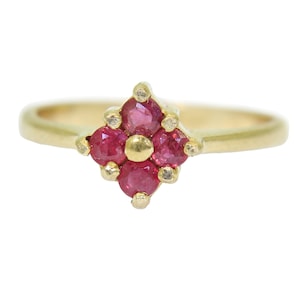 May include: A gold ring with a cluster of six red gemstones set in a flower shape.