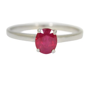 Może przedstawiać: Srebrny pierścionek z czerwonym owalnym rubinem.