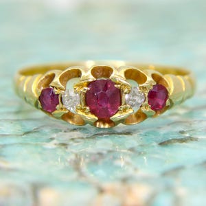 Peut inclure: Une bague en or avec trois rubis rouges et deux diamants sertis dans un design délicat et orné.