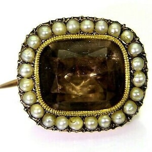 May include: A gold brooch with a large, faceted, brown gemstone surrounded by a border of small, white pearls.